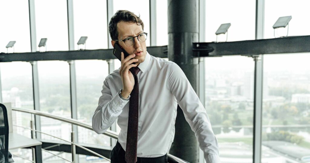 Hombre realizando llamada desde su teléfono celular usando la telefonía IP para comunicarse con sus clientes fuera de la oficina.